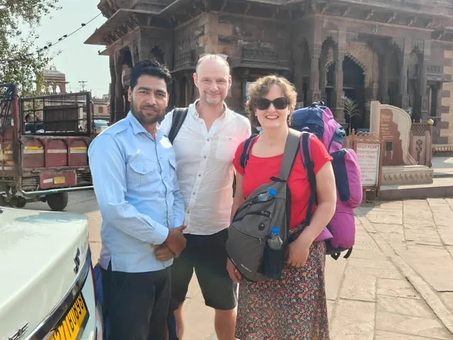 Tour guide and two tourists posing together in front of a stone building
